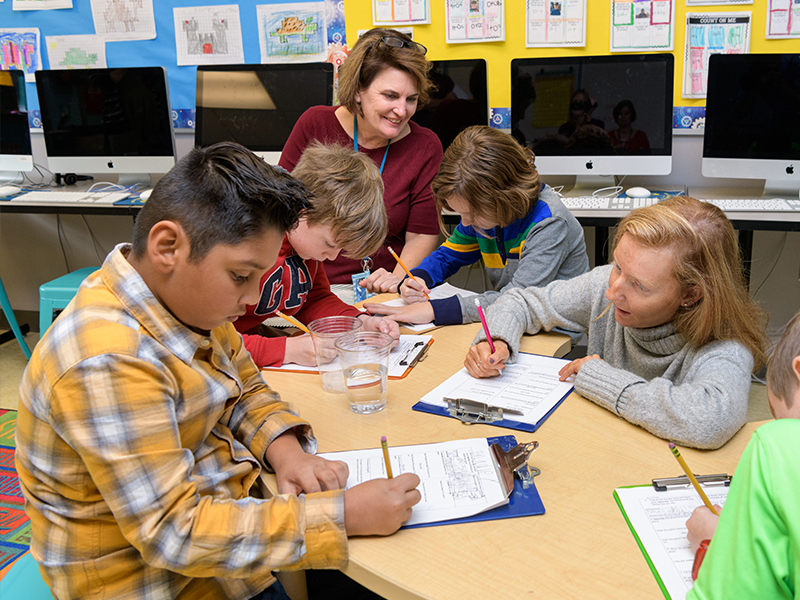 Two teachers help children write notes for science experiment