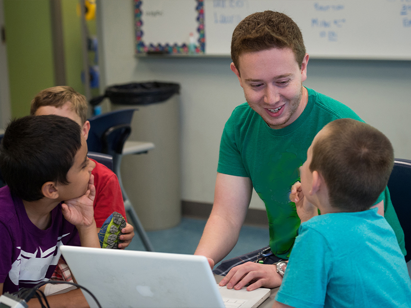 Student teacher with three children doing assignment on a laptop